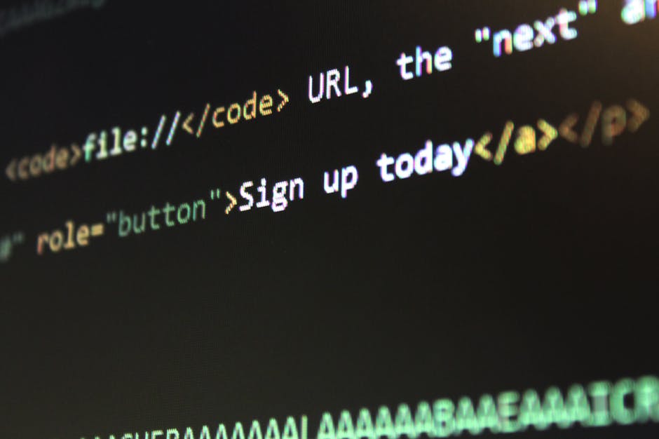 A close-up photograph of a computer screen displaying lines of colorful programming code in multiple colors such as green, purple, blue, and orange against a dark background. The code includes various